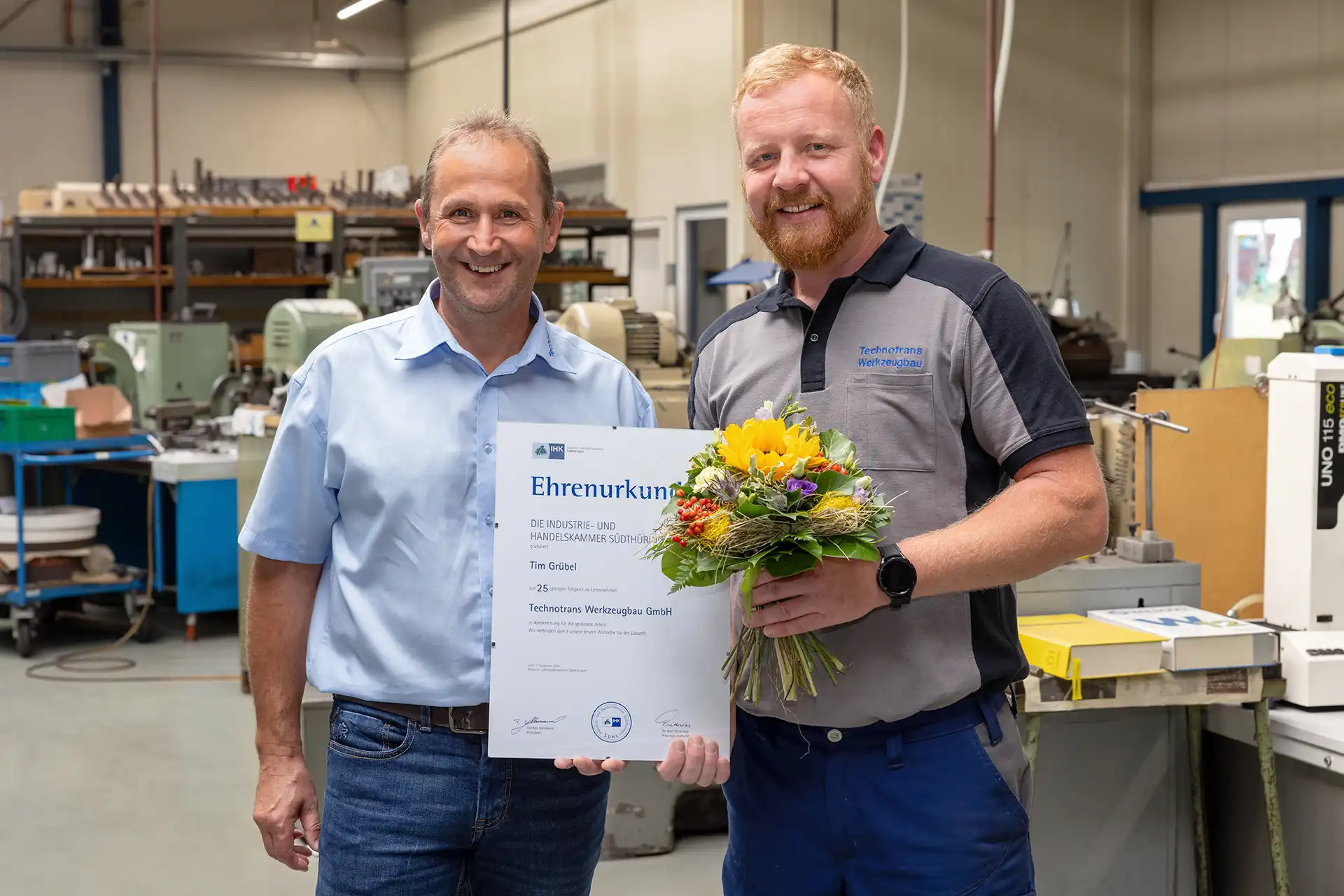 René Liebermann und Tim Grübel lächeln in die Kamera und präsentieren gemeinsam die Ehrenurkunde